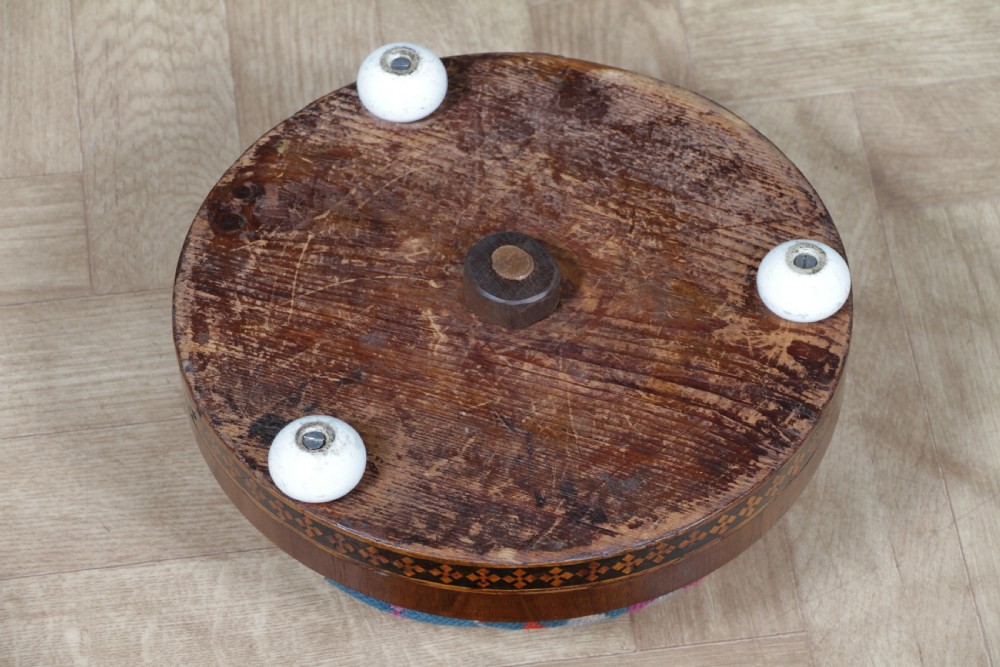 A small round Victorian walnut footstool featuring Tunbridge ware geometric inlay, white ceramic bun feet, and a multi-coloured geometric needlepoint cushion. View VIII