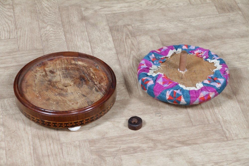 A small round Victorian walnut footstool featuring Tunbridge ware geometric inlay, white ceramic bun feet, and a multi-coloured geometric needlepoint cushion. View IX