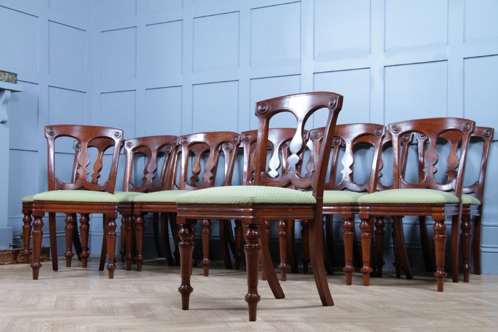 A set of fourteen Victorian mahogany dining chairs featuring carved crown splats, turned front legs, and green patterned upholstered seats. View II
