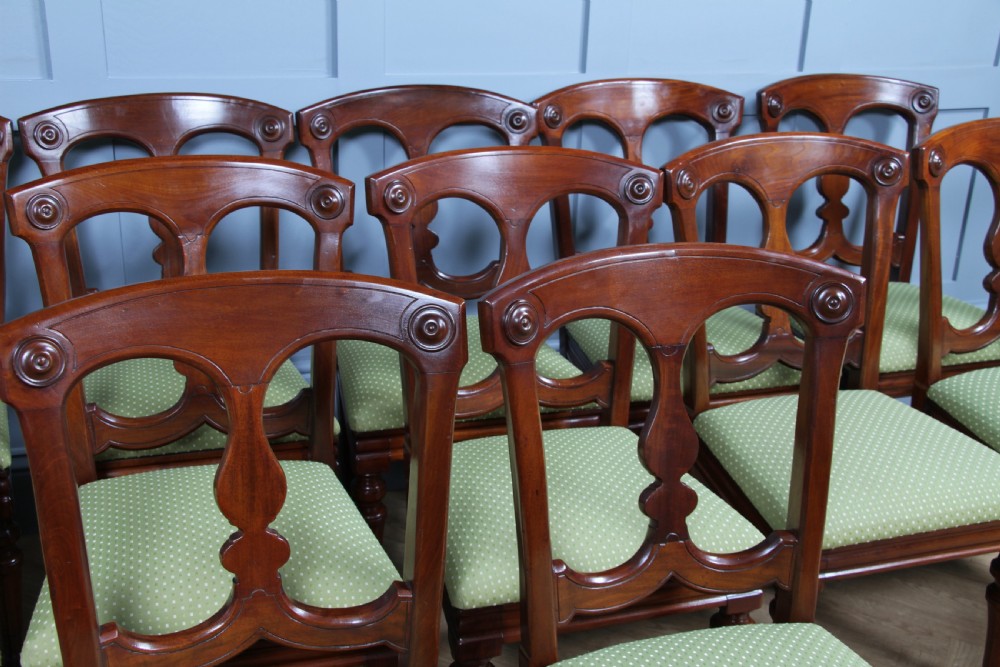 A set of fourteen Victorian mahogany dining chairs featuring carved crown splats, turned front legs, and green patterned upholstered seats. View V