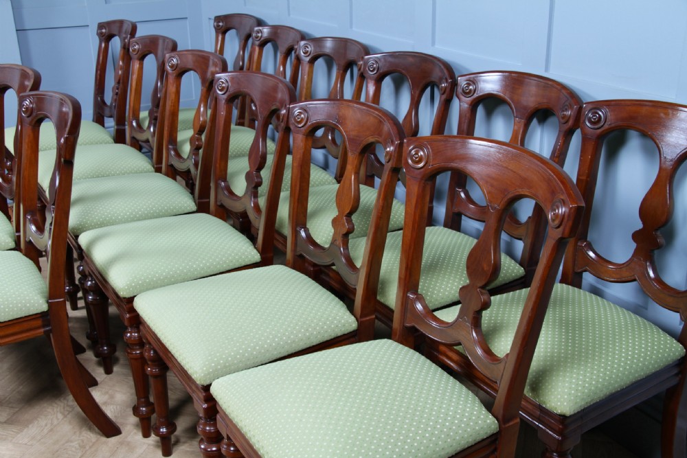 A set of fourteen Victorian mahogany dining chairs featuring carved crown splats, turned front legs, and green patterned upholstered seats. View VI