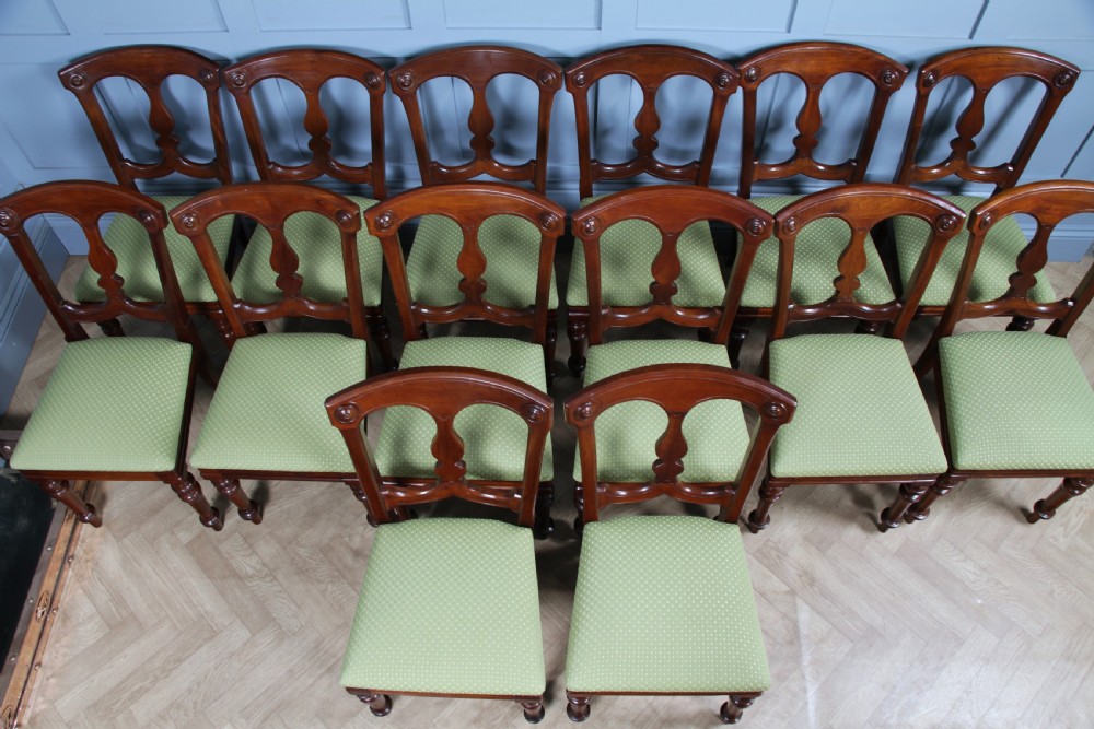 A set of fourteen Victorian mahogany dining chairs featuring carved crown splats, turned front legs, and green patterned upholstered seats. View IX