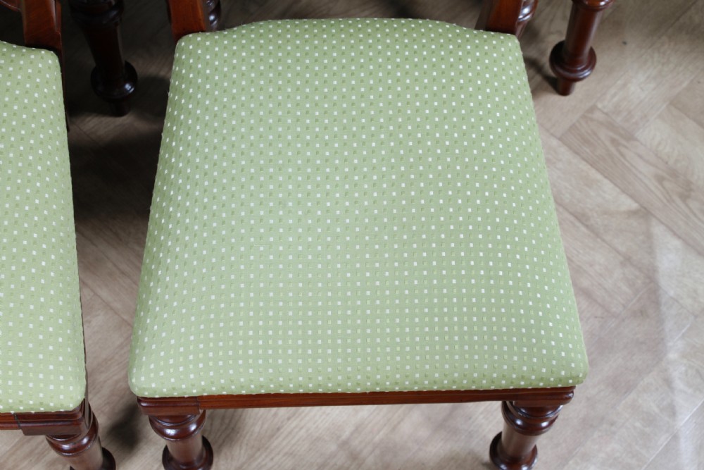 A set of fourteen Victorian mahogany dining chairs featuring carved crown splats, turned front legs, and green patterned upholstered seats. View X