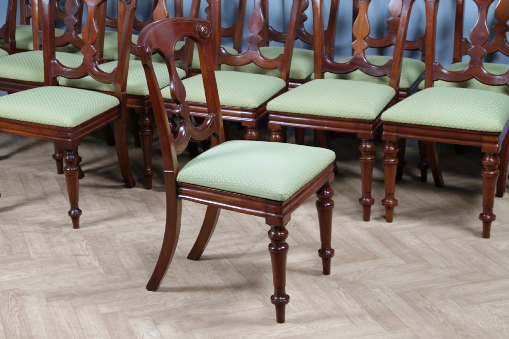 A set of fourteen Victorian mahogany dining chairs featuring carved crown splats, turned front legs, and green patterned upholstered seats. View XV