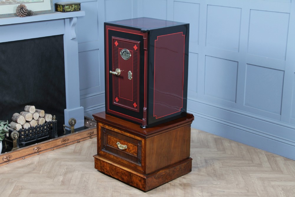A restored black and burgundy Victorian Chubb safe with brass hardware resting atop a dark burr walnut wooden stand with a single drawer. View XV