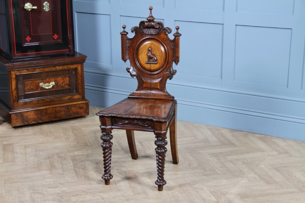 An antique carved dark oak hall chair featuring a decorative backrest with a central crest motif, finials, and barley twist front legs.