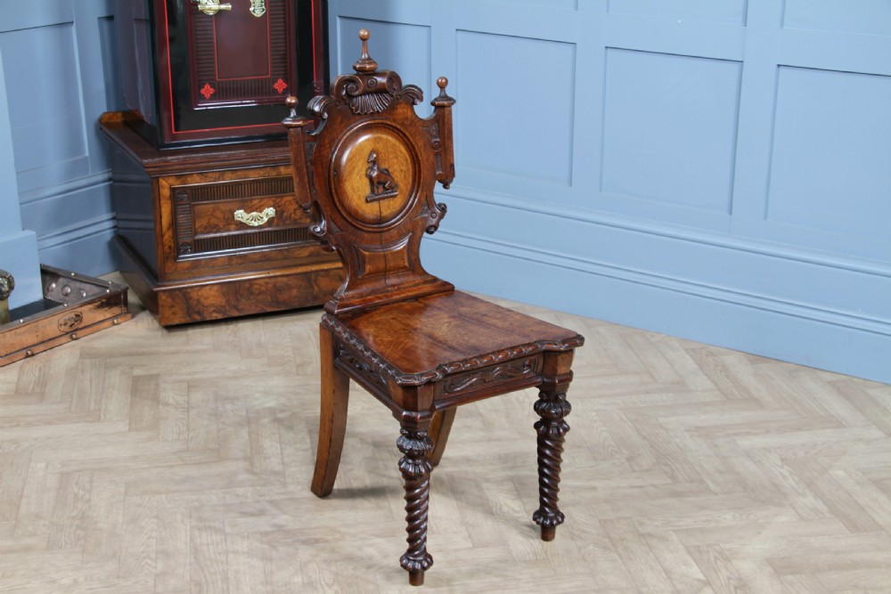 An antique carved dark oak hall chair featuring a decorative backrest with a central crest motif, finials, and barley twist front legs. View II