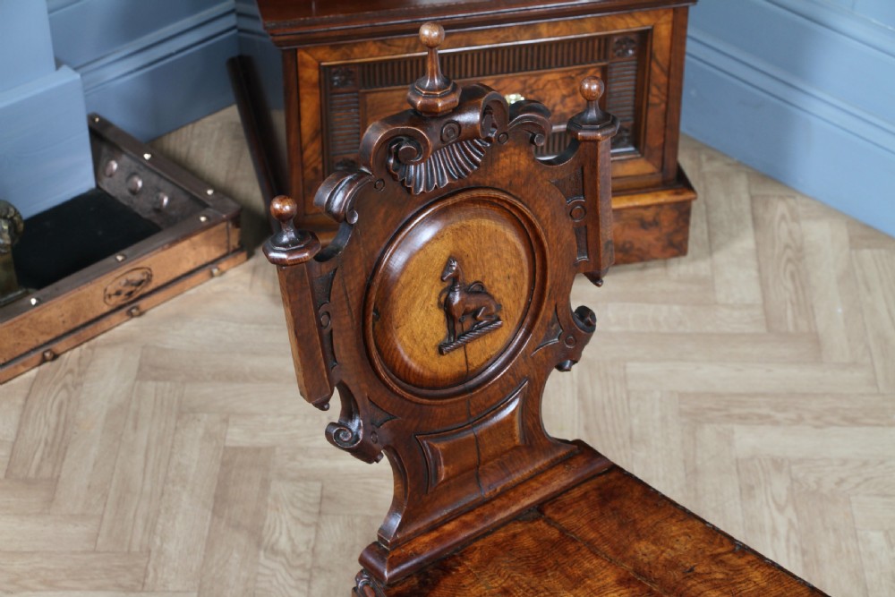 An antique carved dark oak hall chair featuring a decorative backrest with a central crest motif, finials, and barley twist front legs. View III