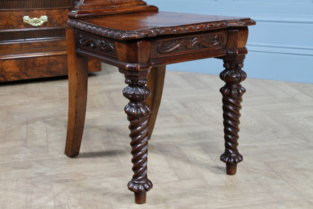 An antique carved dark oak hall chair featuring a decorative backrest with a central crest motif, finials, and barley twist front legs. View V