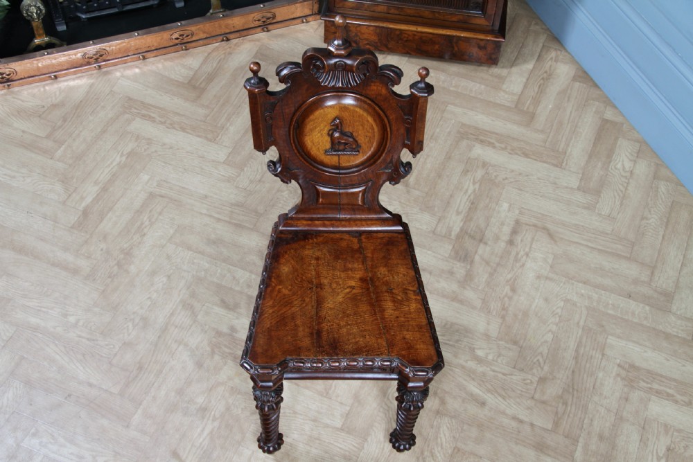 An antique carved dark oak hall chair featuring a decorative backrest with a central crest motif, finials, and barley twist front legs. View VI