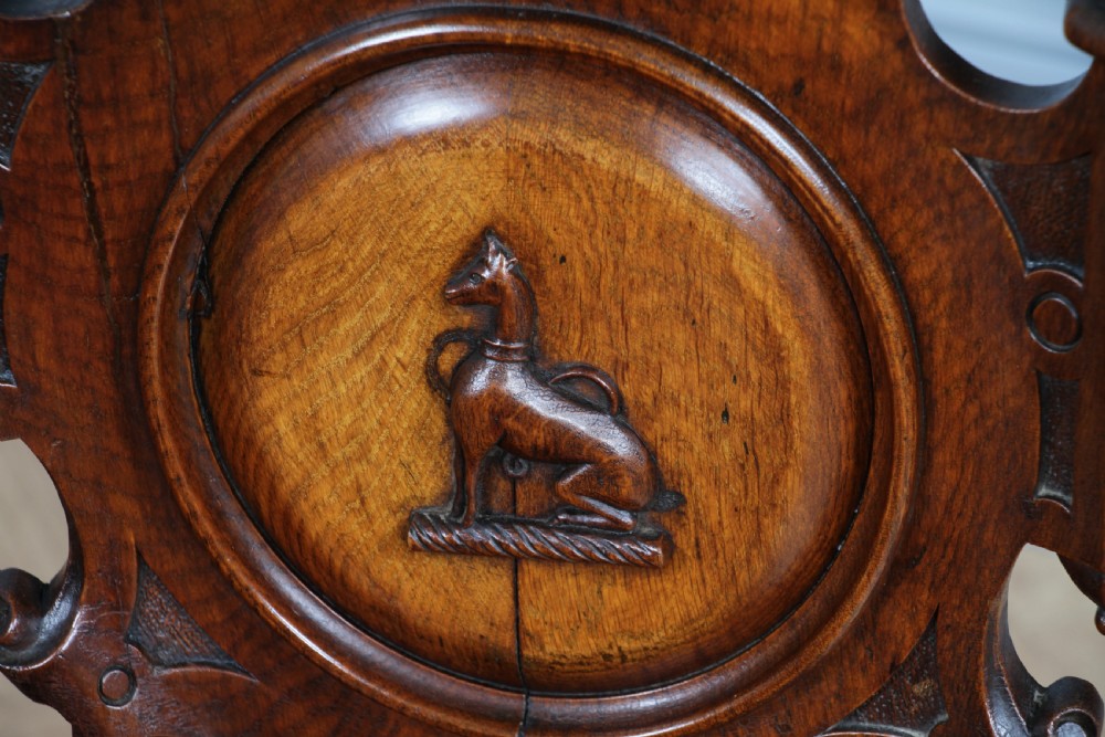 An antique carved dark oak hall chair featuring a decorative backrest with a central crest motif, finials, and barley twist front legs. View VII