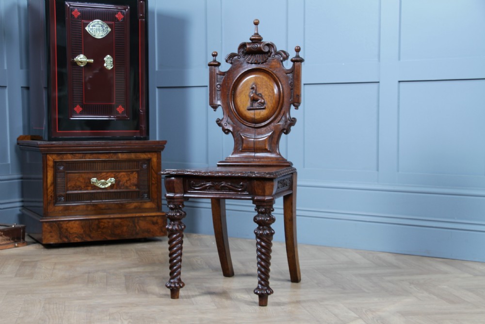 An antique carved dark oak hall chair featuring a decorative backrest with a central crest motif, finials, and barley twist front legs. View IX