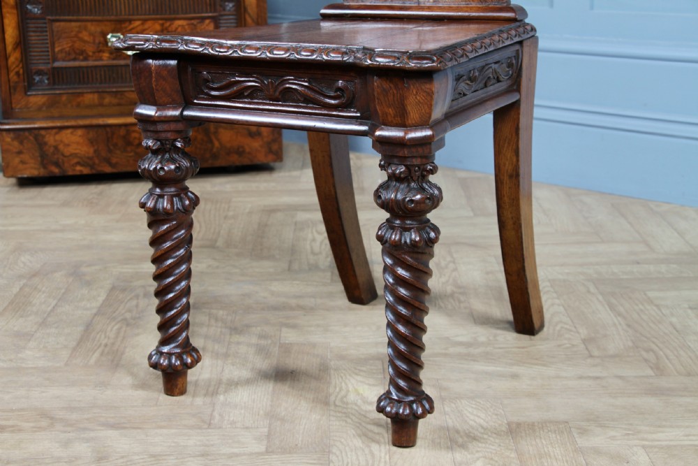 An antique carved dark oak hall chair featuring a decorative backrest with a central crest motif, finials, and barley twist front legs. View XI