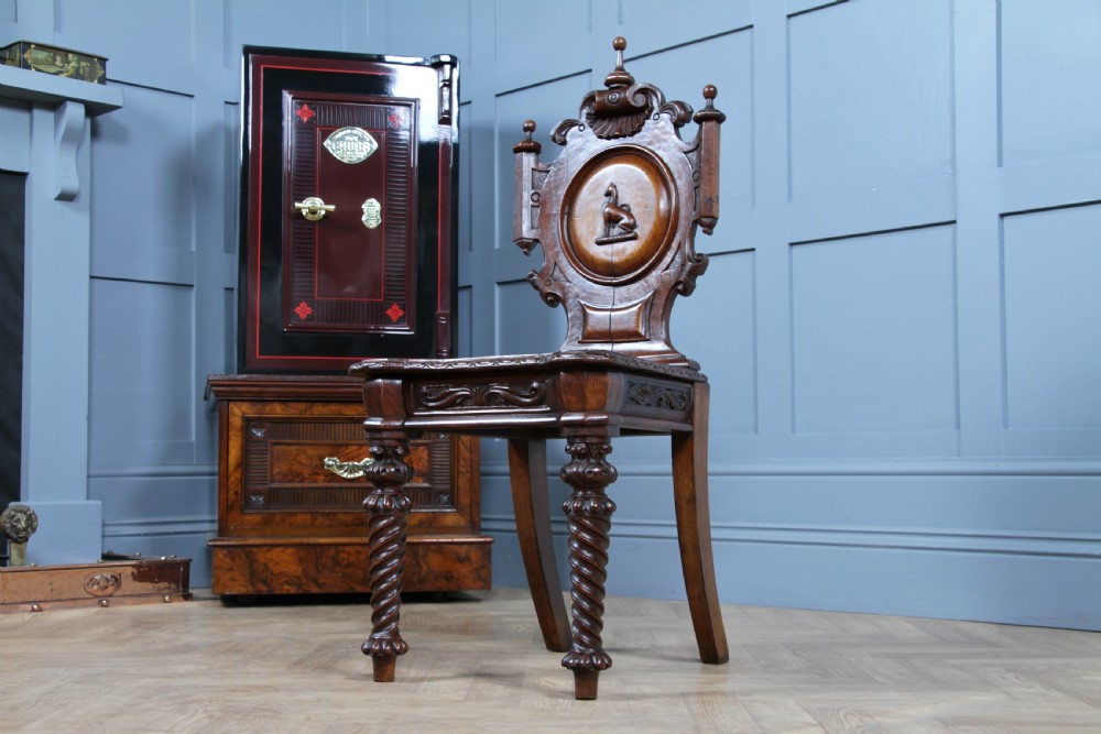 An antique carved dark oak hall chair featuring a decorative backrest with a central crest motif, finials, and barley twist front legs. View XII