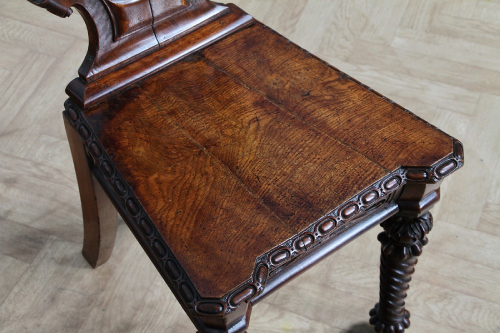 An antique carved dark oak hall chair featuring a decorative backrest with a central crest motif, finials, and barley twist front legs. View XIII