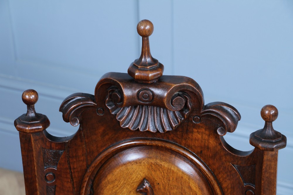 An antique carved dark oak hall chair featuring a decorative backrest with a central crest motif, finials, and barley twist front legs. View XIV