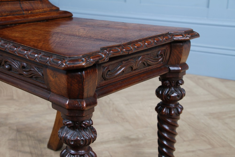 An antique carved dark oak hall chair featuring a decorative backrest with a central crest motif, finials, and barley twist front legs. View XV