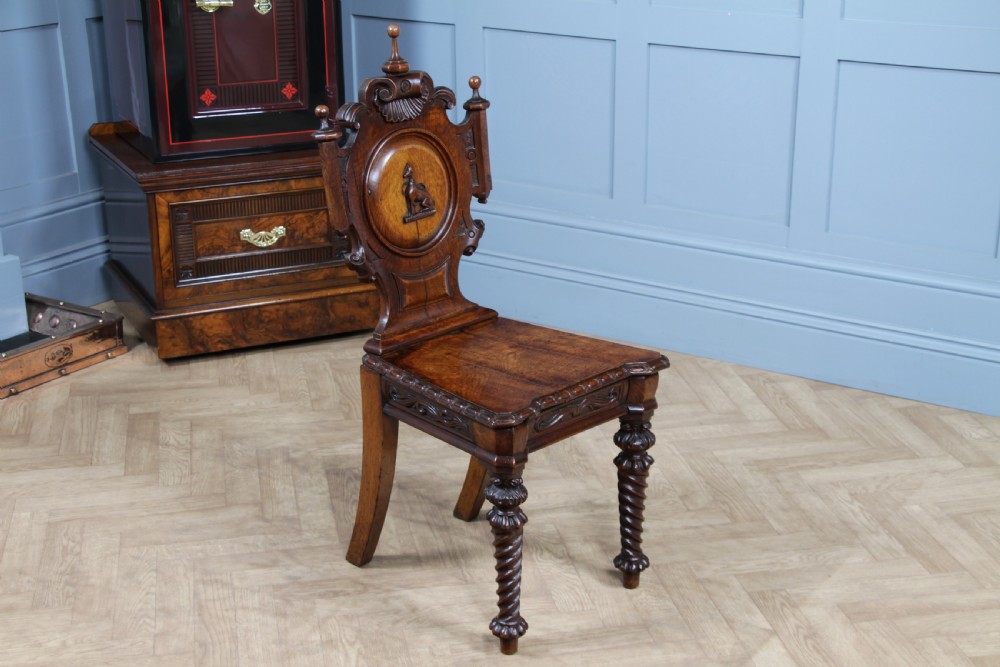 An antique carved dark oak hall chair featuring a decorative backrest with a central crest motif, finials, and barley twist front legs. View XVI