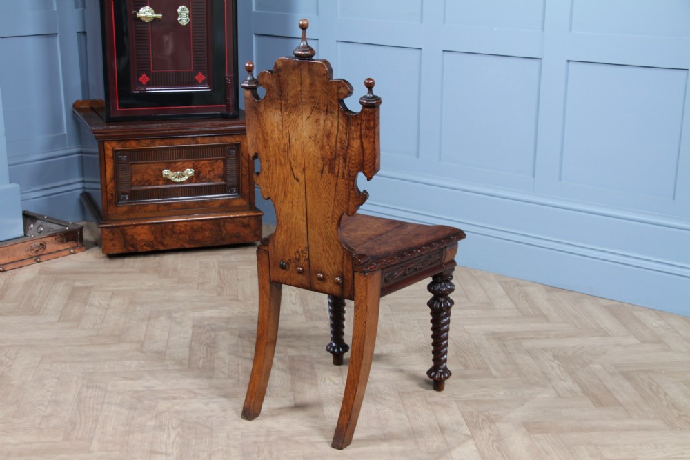 An antique carved dark oak hall chair featuring a decorative backrest with a central crest motif, finials, and barley twist front legs. View XVII