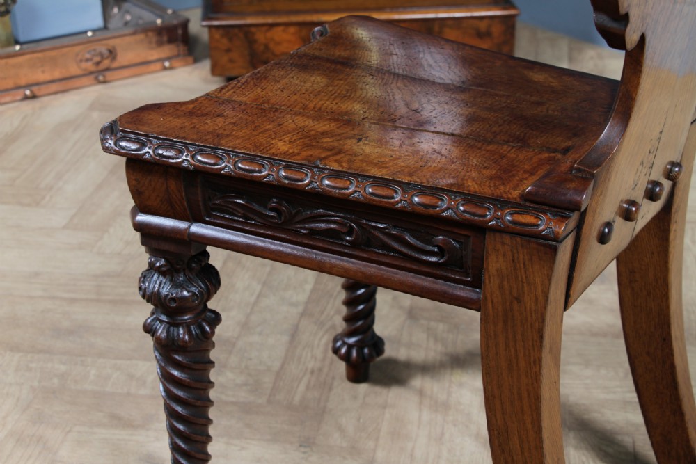 An antique carved dark oak hall chair featuring a decorative backrest with a central crest motif, finials, and barley twist front legs. View XVIII