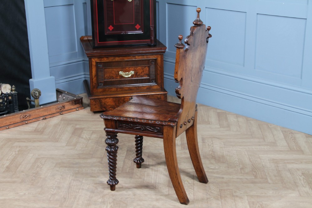 An antique carved dark oak hall chair featuring a decorative backrest with a central crest motif, finials, and barley twist front legs. View XX