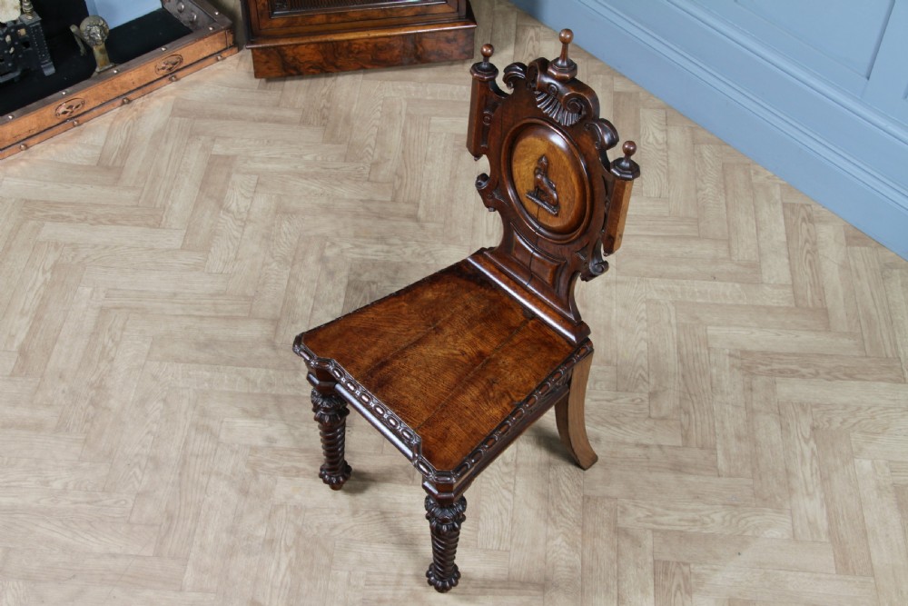 An antique carved dark oak hall chair featuring a decorative backrest with a central crest motif, finials, and barley twist front legs. View XXI