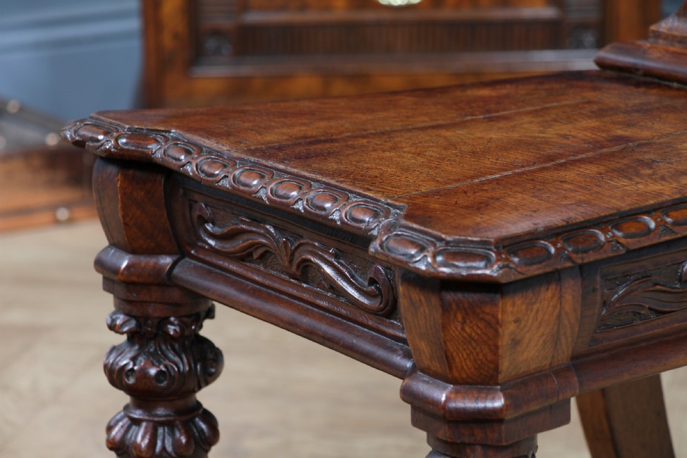 An antique carved dark oak hall chair featuring a decorative backrest with a central crest motif, finials, and barley twist front legs. View XXIII