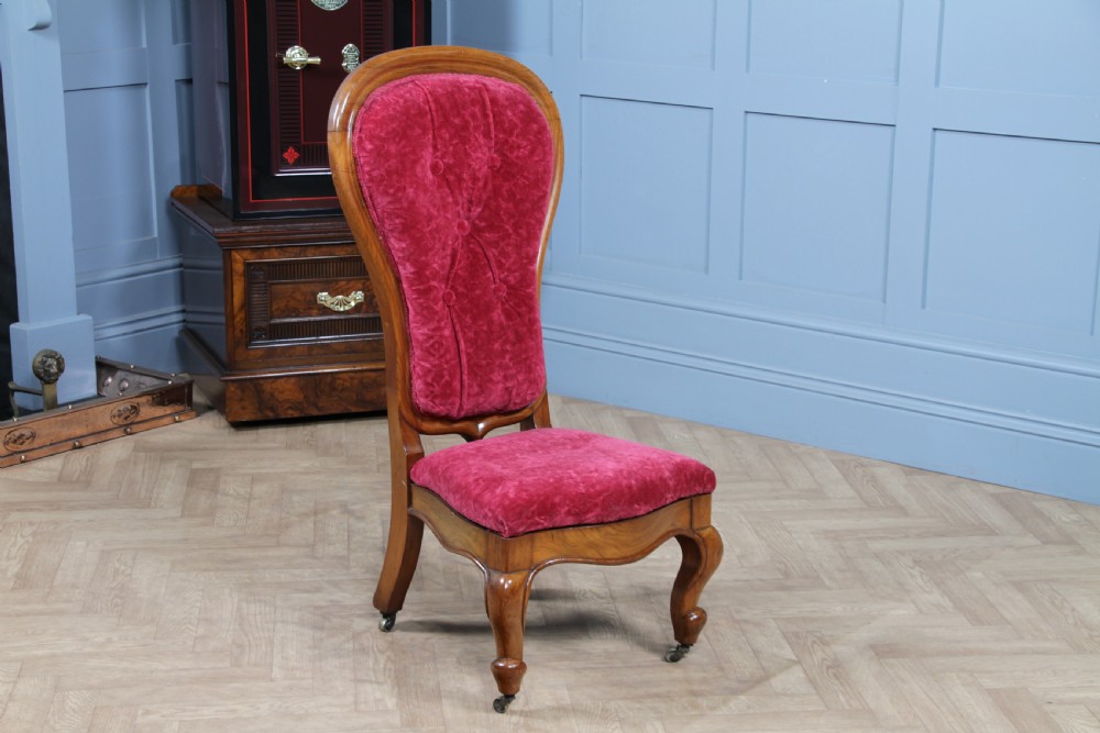 A Victorian walnut nursing chair featuring a tall balloon back with deep-buttoned magenta velvet upholstery and cabriole front legs on brass castors.