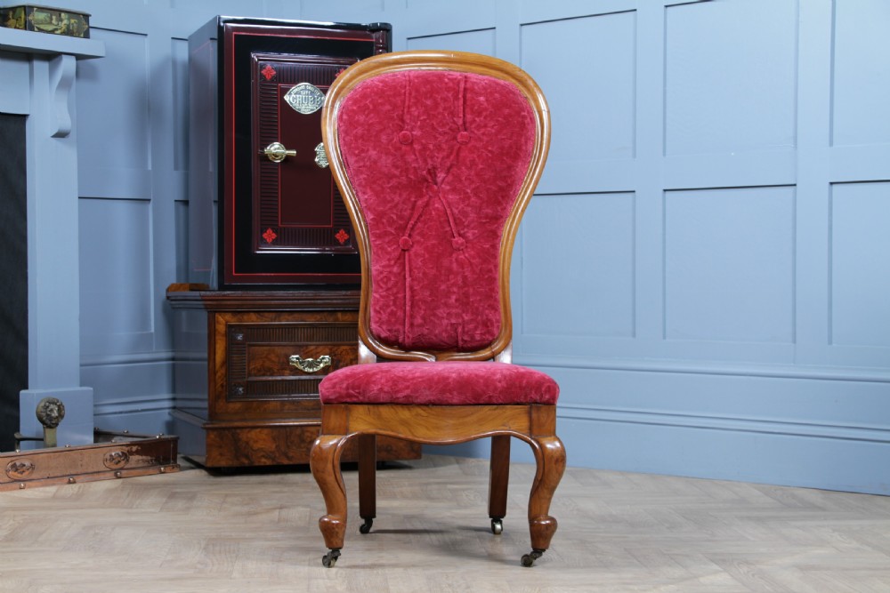A Victorian walnut nursing chair featuring a tall balloon back with deep-buttoned magenta velvet upholstery and cabriole front legs on brass castors. View II