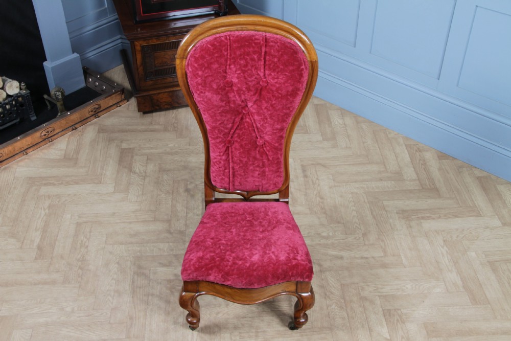 A Victorian walnut nursing chair featuring a tall balloon back with deep-buttoned magenta velvet upholstery and cabriole front legs on brass castors. View III