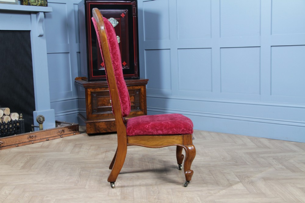 A Victorian walnut nursing chair featuring a tall balloon back with deep-buttoned magenta velvet upholstery and cabriole front legs on brass castors. View V