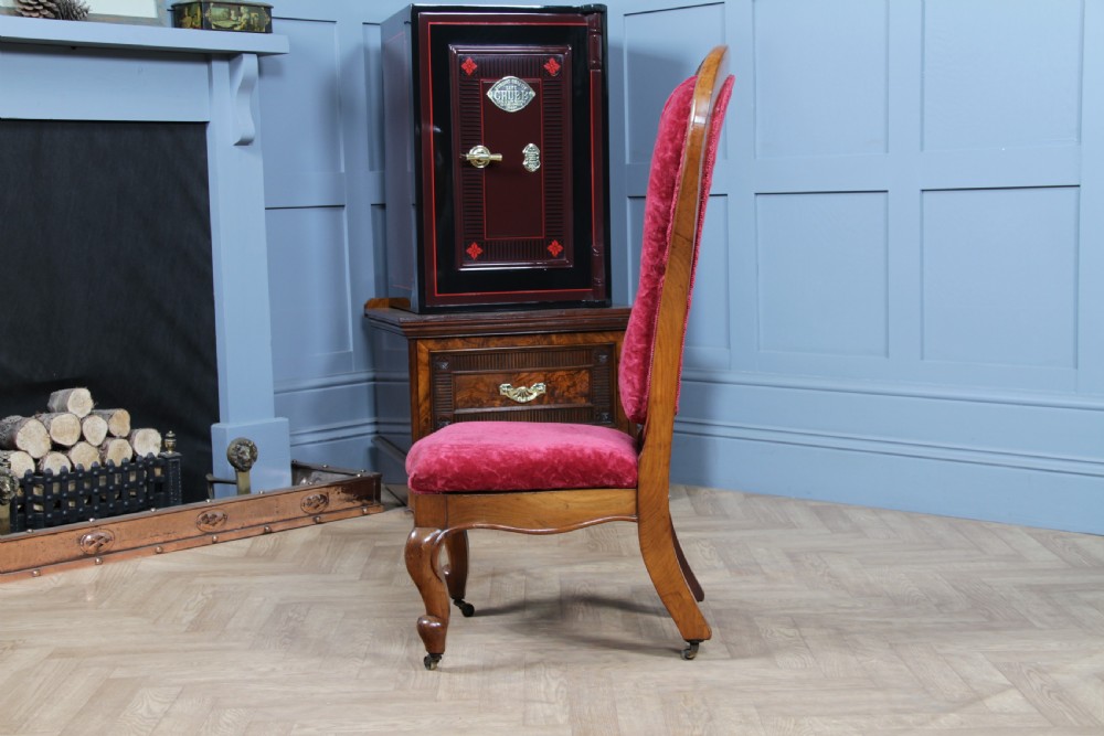 A Victorian walnut nursing chair featuring a tall balloon back with deep-buttoned magenta velvet upholstery and cabriole front legs on brass castors. View VI
