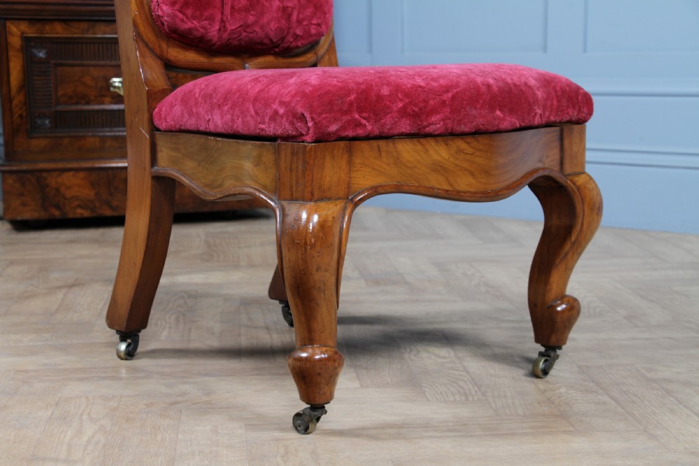 A Victorian walnut nursing chair featuring a tall balloon back with deep-buttoned magenta velvet upholstery and cabriole front legs on brass castors. View VII