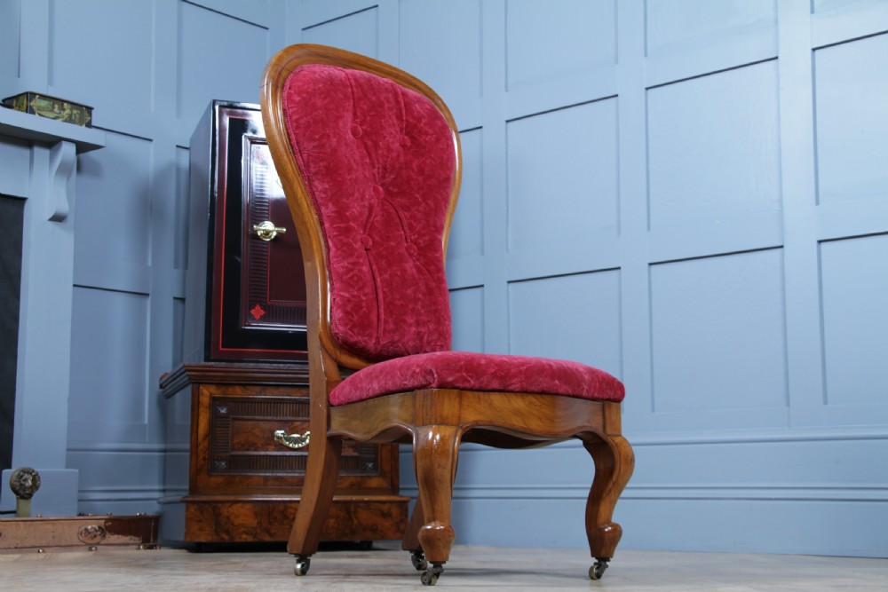 A Victorian walnut nursing chair featuring a tall balloon back with deep-buttoned magenta velvet upholstery and cabriole front legs on brass castors. View VIII