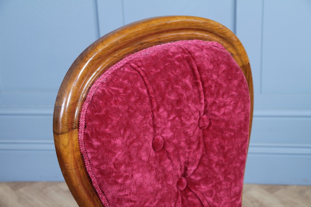 A Victorian walnut nursing chair featuring a tall balloon back with deep-buttoned magenta velvet upholstery and cabriole front legs on brass castors. View X