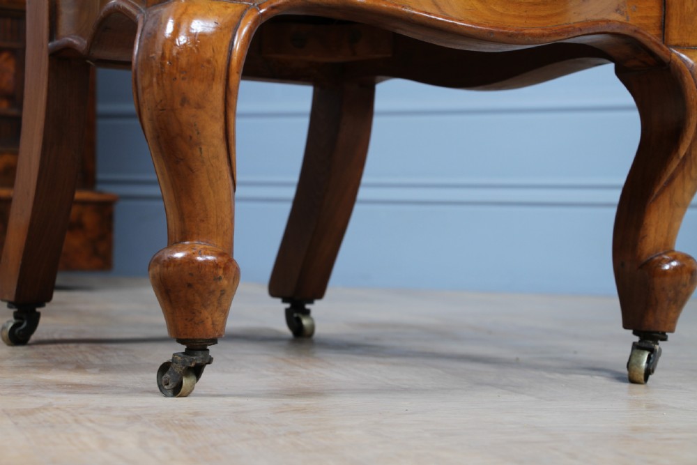 A Victorian walnut nursing chair featuring a tall balloon back with deep-buttoned magenta velvet upholstery and cabriole front legs on brass castors. View XII