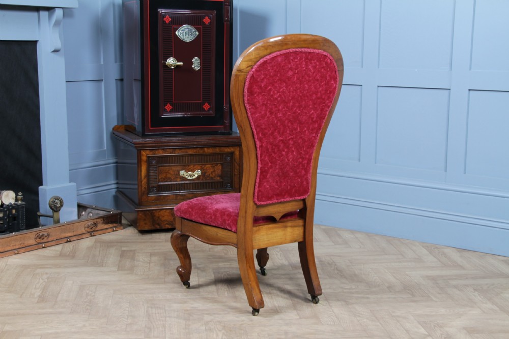 A Victorian walnut nursing chair featuring a tall balloon back with deep-buttoned magenta velvet upholstery and cabriole front legs on brass castors. View XIII