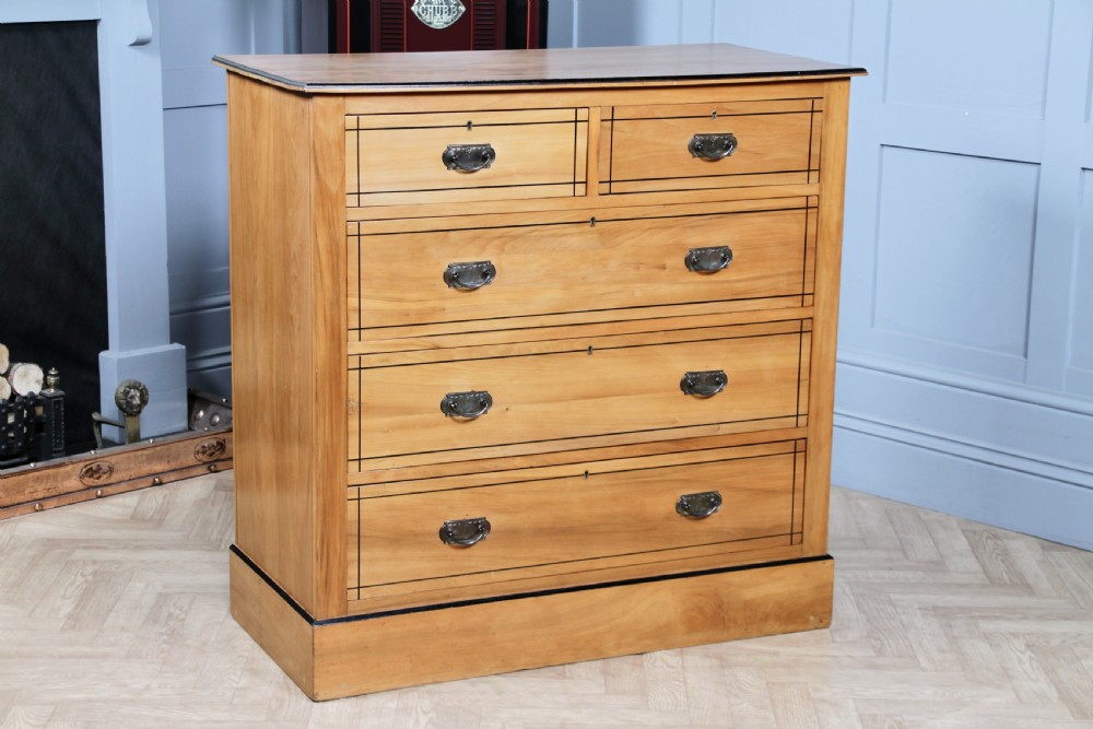 A late Victorian satinwood chest featuring two short drawers above three long drawers with ebonised stringing and dark metal handles on a solid plinth base.