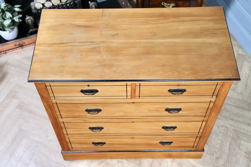 A late Victorian satinwood chest featuring two short drawers above three long drawers with ebonised stringing and dark metal handles on a solid plinth base. View V