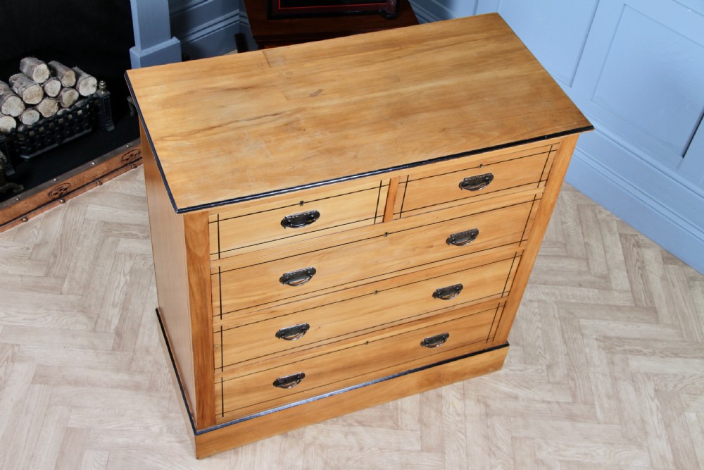 A late Victorian satinwood chest featuring two short drawers above three long drawers with ebonised stringing and dark metal handles on a solid plinth base. View VI