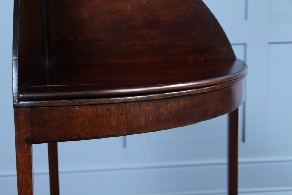 An antique dark mahogany corner washstand featuring a curved splashback with a small top shelf, a middle surface tier, a lower shelf with a central drawer, and splayed legs. View VI