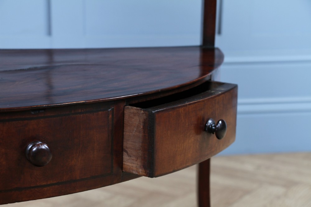 An antique dark mahogany corner washstand featuring a curved splashback with a small top shelf, a middle surface tier, a lower shelf with a central drawer, and splayed legs. View VII
