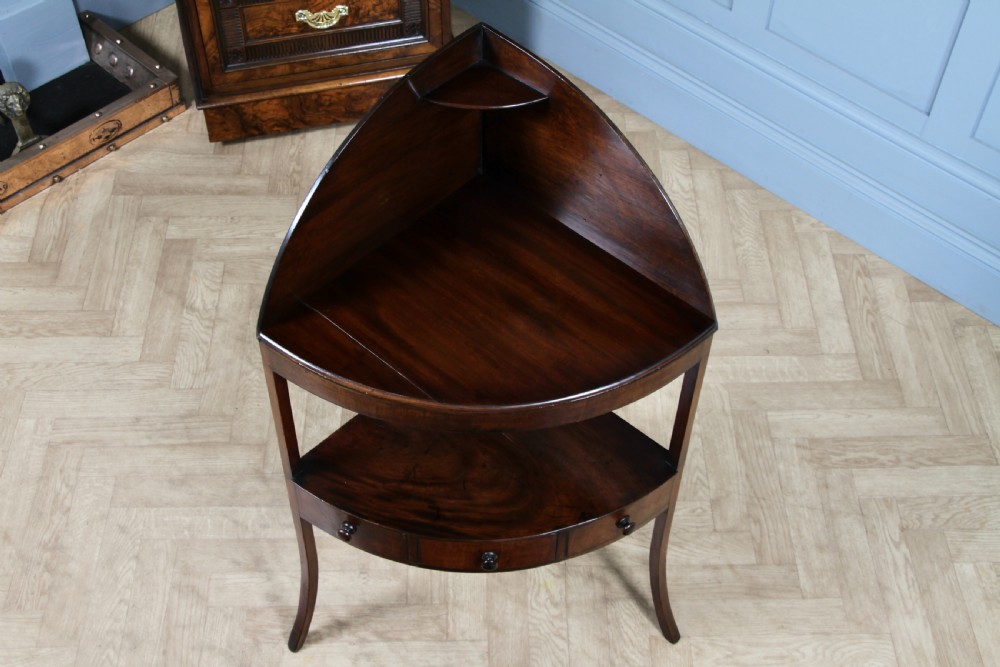 An antique dark mahogany corner washstand featuring a curved splashback with a small top shelf, a middle surface tier, a lower shelf with a central drawer, and splayed legs. View IX