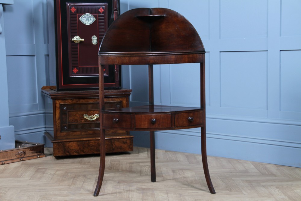 An antique dark mahogany corner washstand featuring a curved splashback with a small top shelf, a middle surface tier, a lower shelf with a central drawer, and splayed legs. View XII