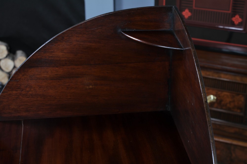 An antique dark mahogany corner washstand featuring a curved splashback with a small top shelf, a middle surface tier, a lower shelf with a central drawer, and splayed legs. View XIV