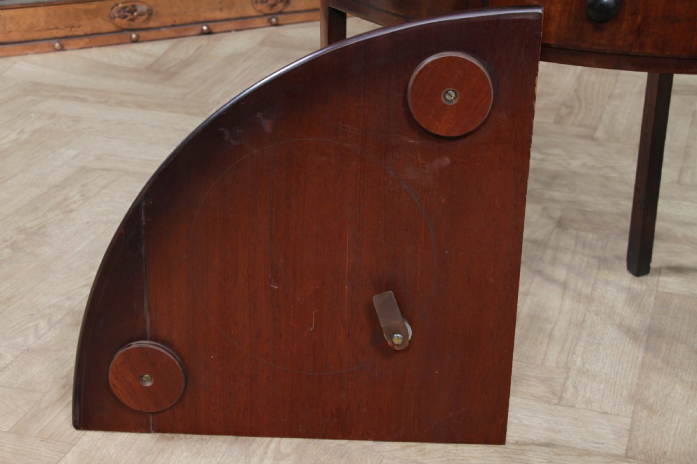 An antique dark mahogany corner washstand featuring a curved splashback with a small top shelf, a middle surface tier, a lower shelf with a central drawer, and splayed legs. View XX