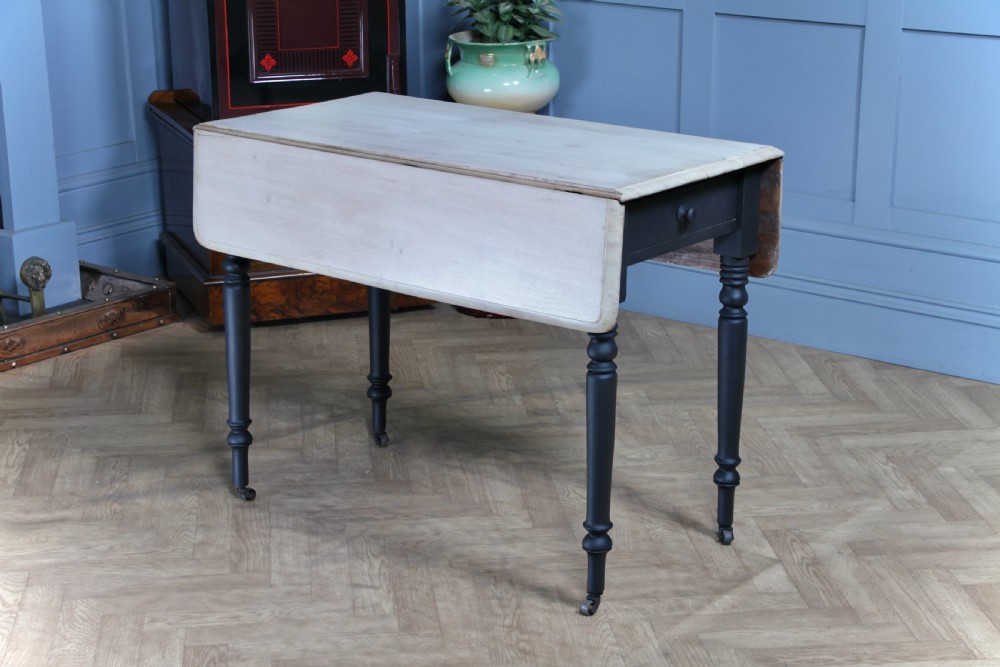A restored Victorian Pembroke table featuring a bleached mahogany drop-leaf top and a black painted frame with turned legs on brass castors.