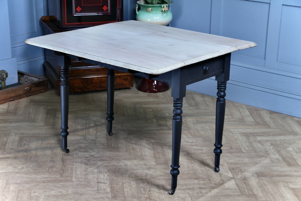 A restored Victorian Pembroke table featuring a bleached mahogany drop-leaf top and a black painted frame with turned legs on brass castors. View III