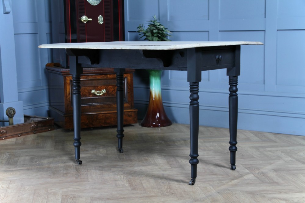 A restored Victorian Pembroke table featuring a bleached mahogany drop-leaf top and a black painted frame with turned legs on brass castors. View V