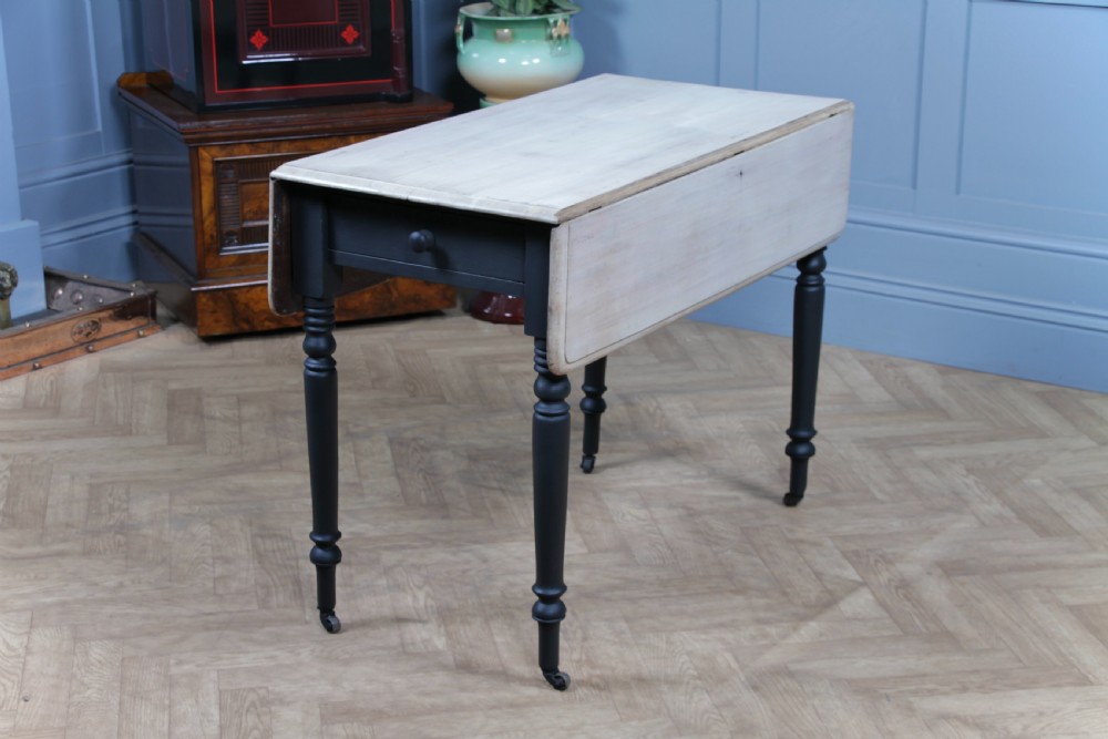 A restored Victorian Pembroke table featuring a bleached mahogany drop-leaf top and a black painted frame with turned legs on brass castors. View VI